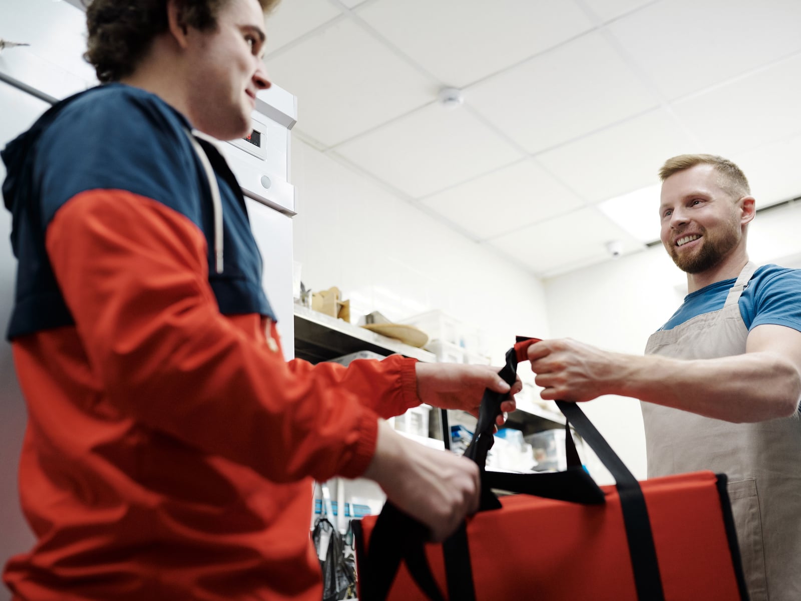 A courier collecting a packed order from a cook at the counter