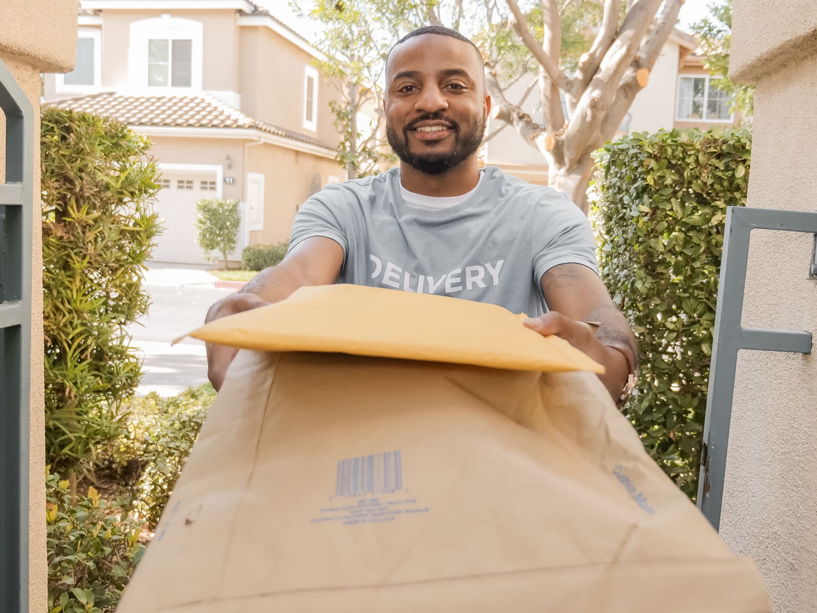 A smiling delivery man handing a parcel to a customer at their gate